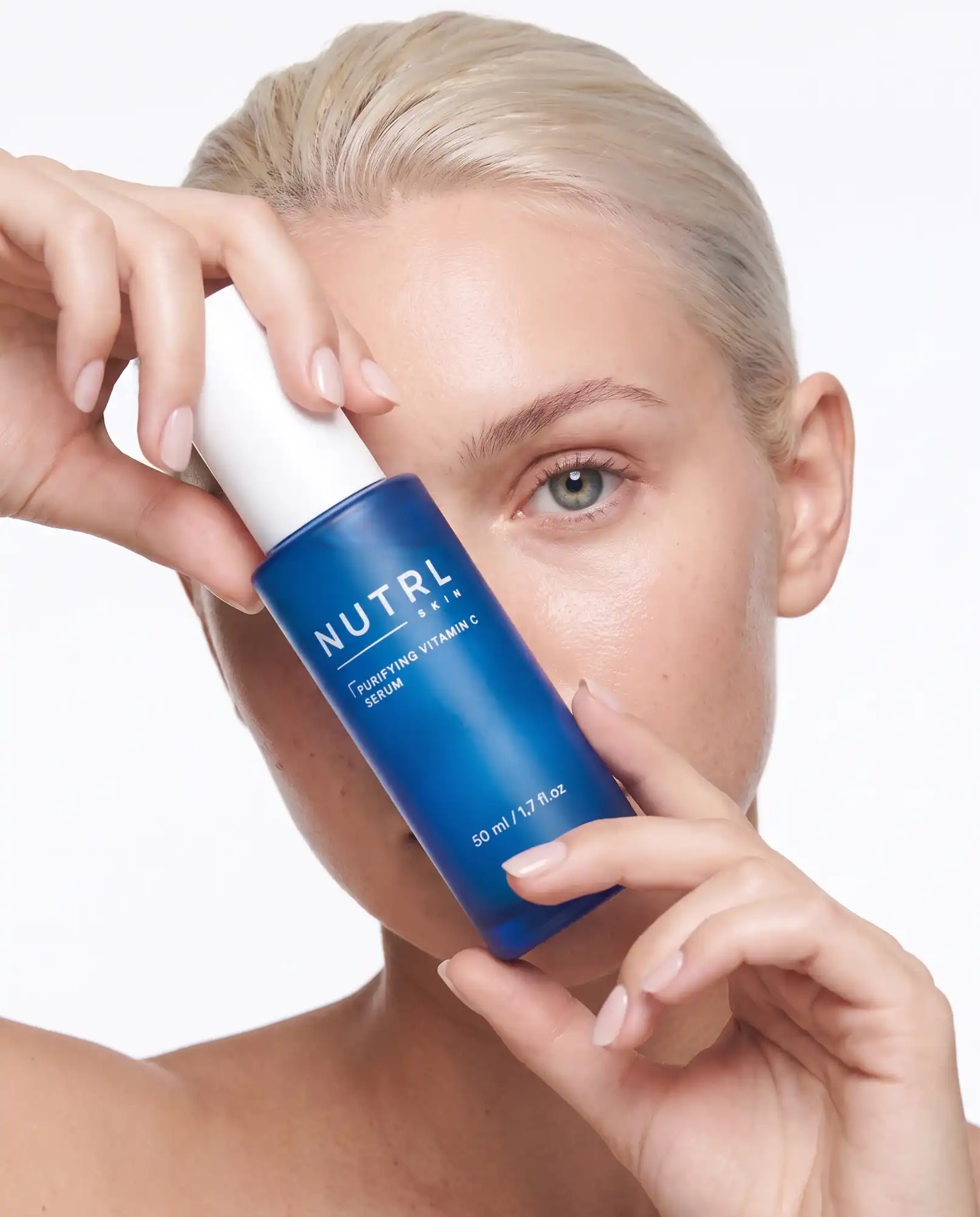 Woman holding a NUTRL Purifying Vitamin C Serum bottle next to her face