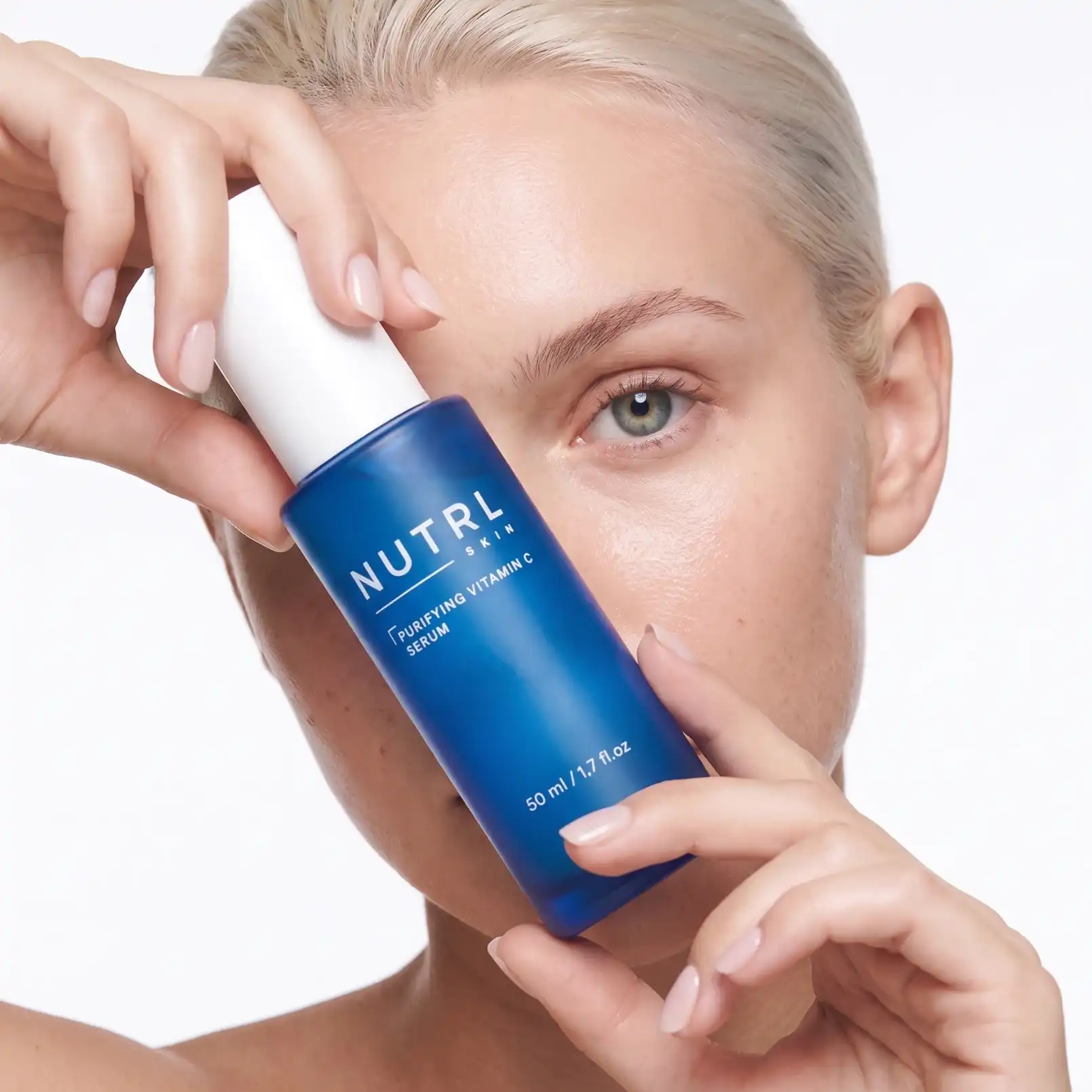 Woman holding a NUTRL Purifying Vitamin C Serum bottle next to her face