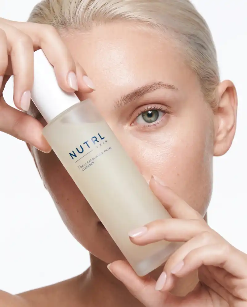 Woman holding a NUTRL Daily Exfoliating Facial Cleanser bottle next to her face